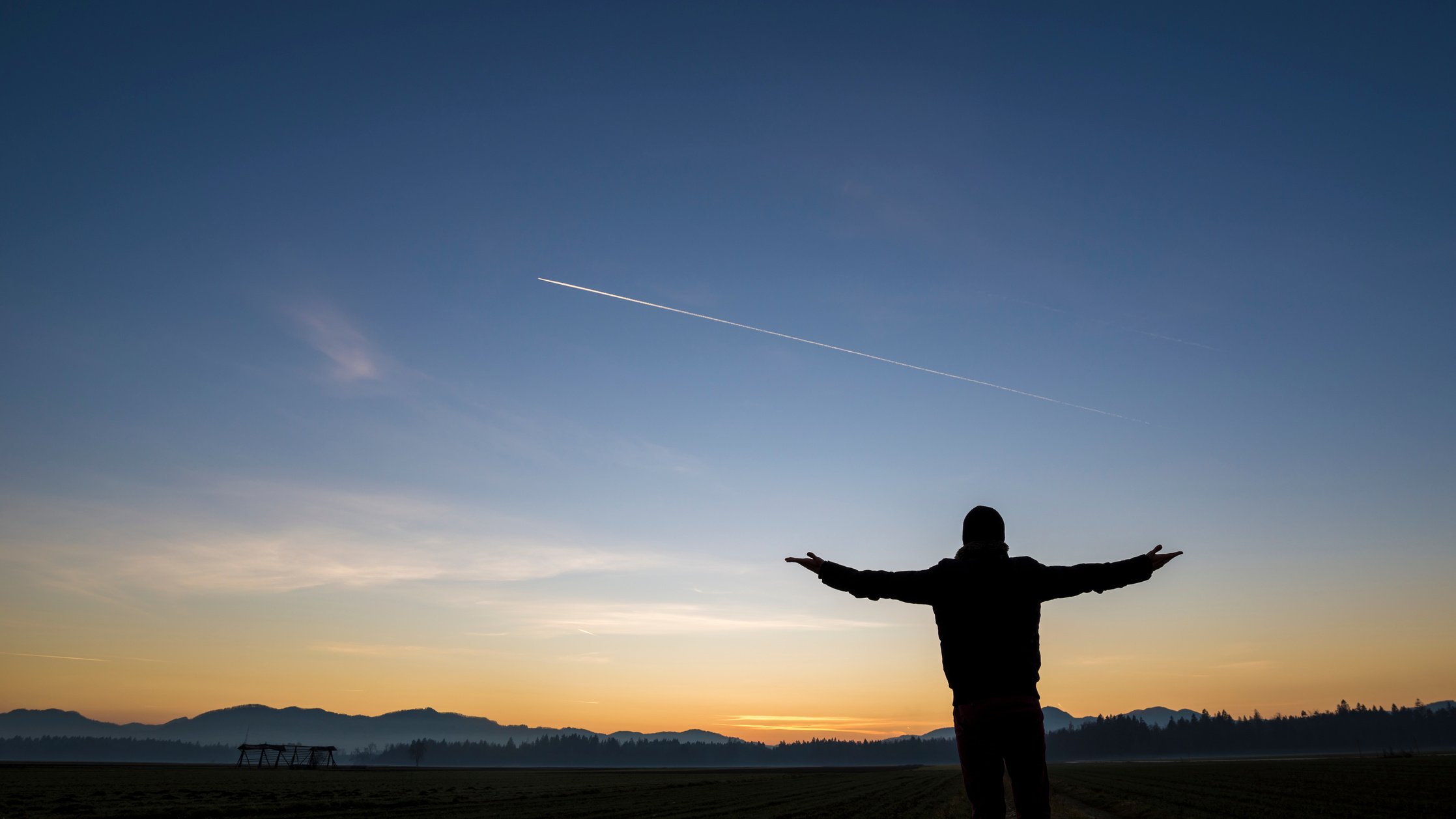 Silhouetter of a Man Standing and Airplane Trail Across the Sky